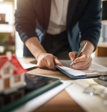 Signature d’un document de gestion immobilière devant une maquette de maison, pour une SCI ou un loueur LMNP